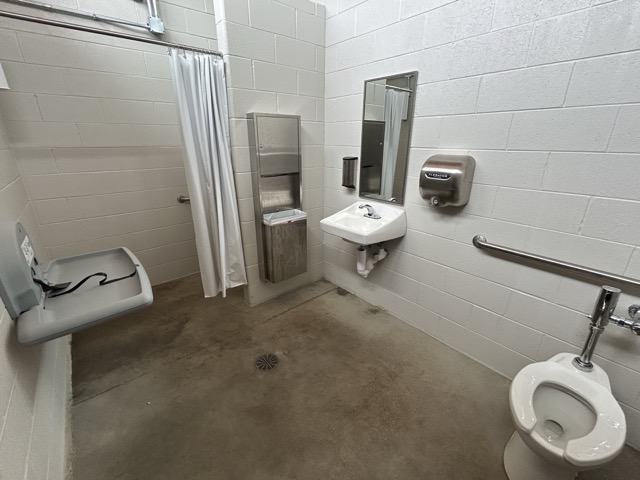 Shows shower, changing table, sink, and toilet in family changing area at the splash pad at Lil's Park.