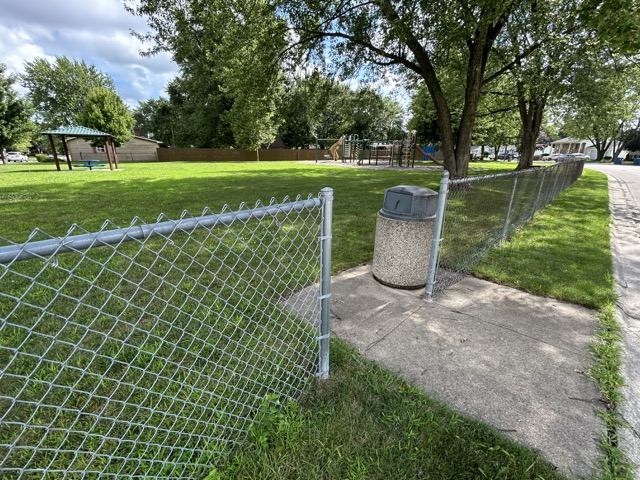 Playground equipment, a fence with openings, and a trash bin at the park in Bourbonnais.