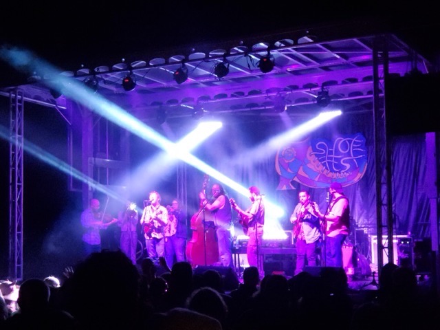 Festival audience watching live music at Shoe Fest, from twilight to night with stage lights glowing.