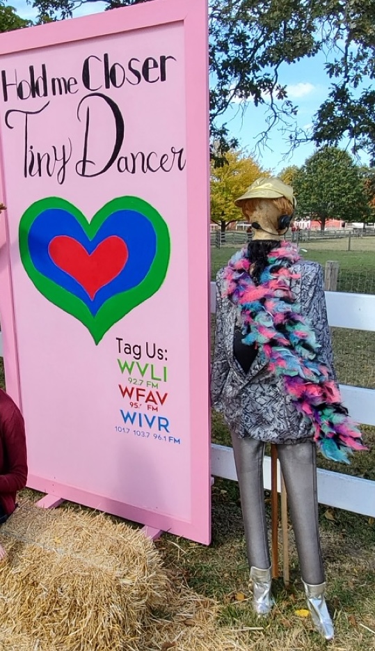 Scarecrow dressed as a playful dancer with a sign that reads ‘Hold Me Closer Tiny Dancer,’ created by Milner Media Partners, a local radio station group.