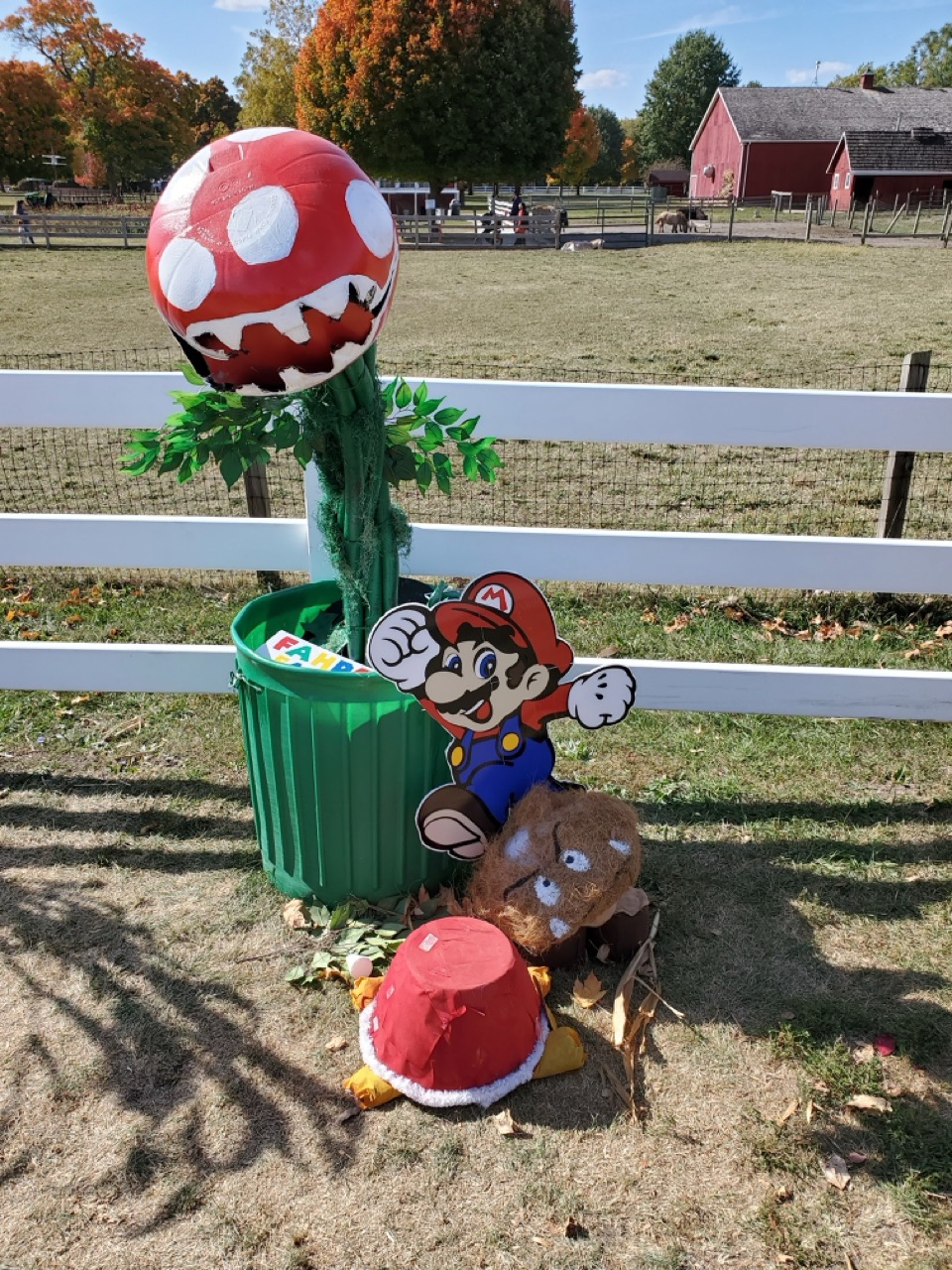 Three creative scarecrows: one dressed as Mario, one shaped like a school bus, and one traditional scarecrow wearing a Tholen’s shirt from a local business.